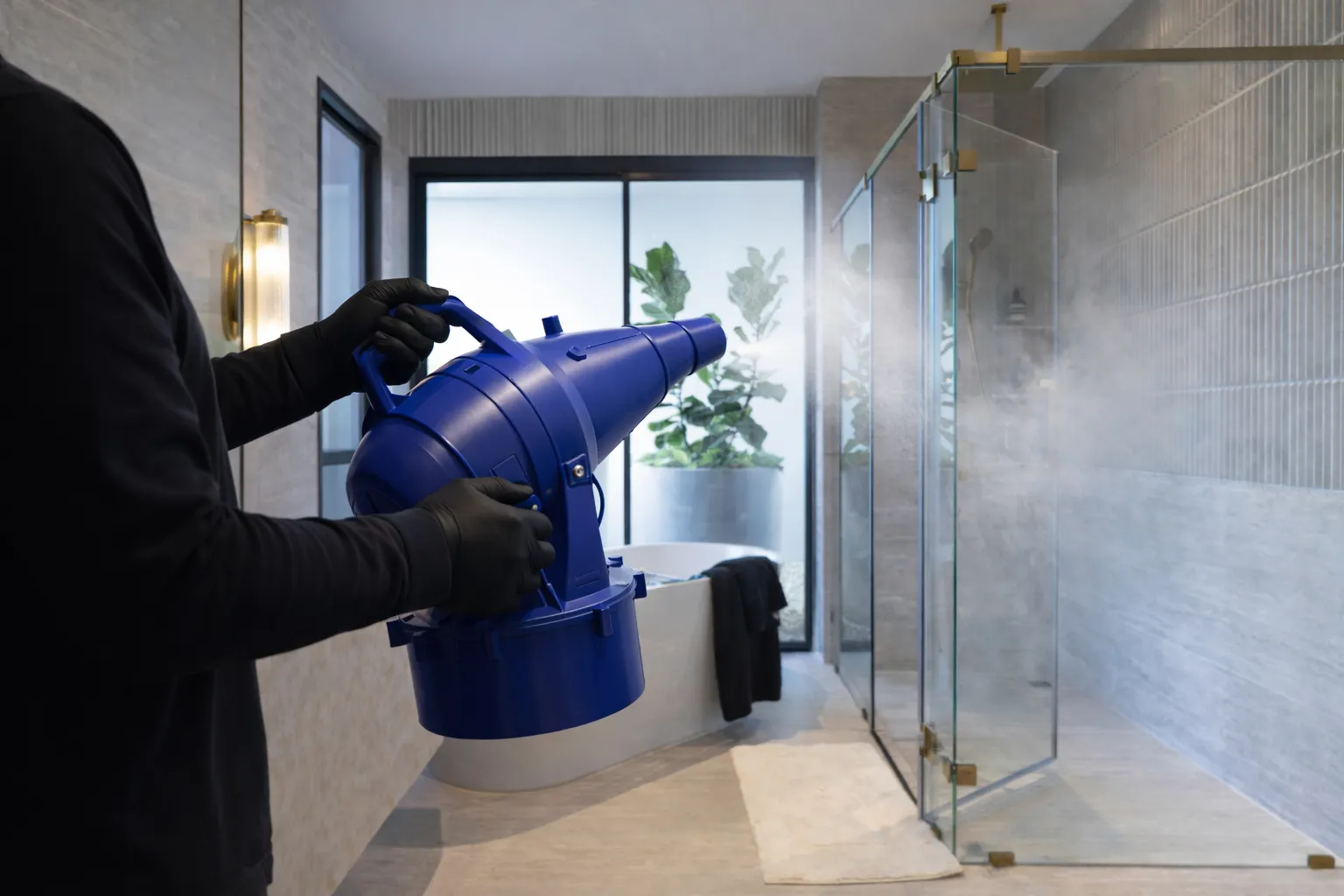 Technician using commercial fogging device to disperse SAN-AIR treatment in modern bathroom